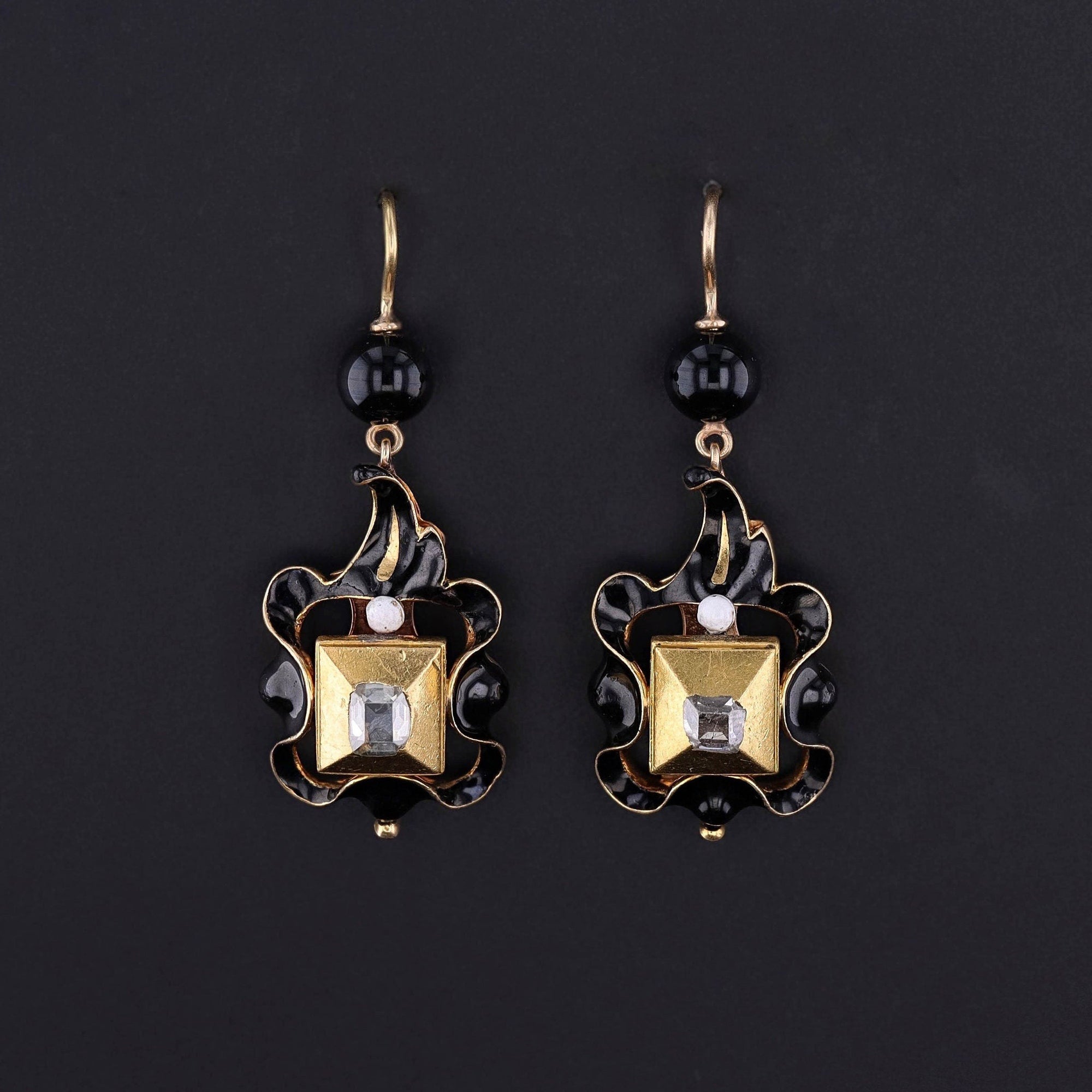A rare pair of 17th century table cut diamond dangles in 22ct rub over settings with 18k black and white enamel drops, leaded glass bead surmounts, and 14k gold ear wires.