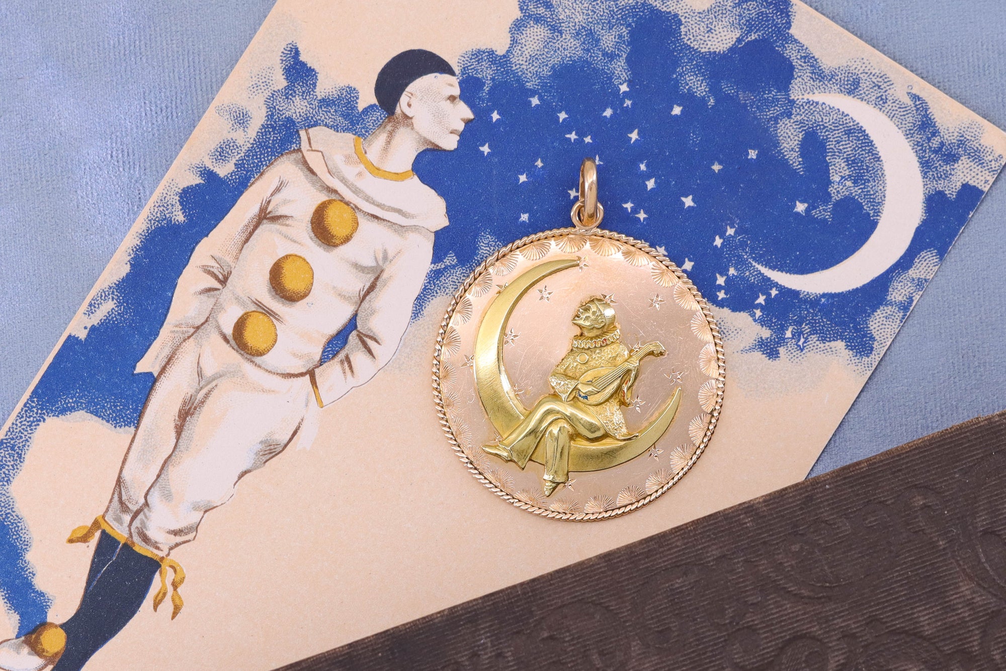 A large antique pendant depicting Pierrot the clown on a crescent of gold strumming a manodlin.