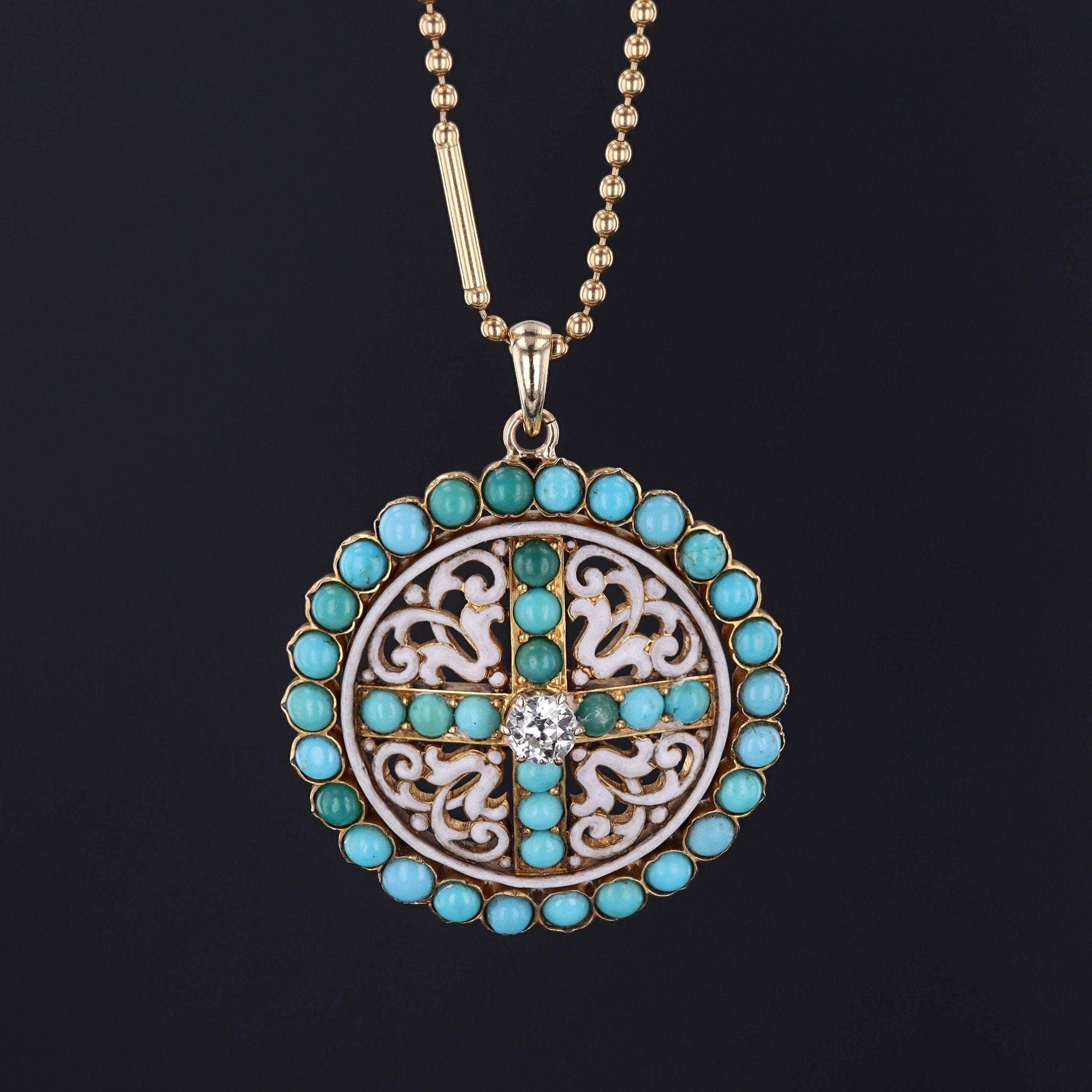 A round, antique pendant necklace with blue turquoise cabochons and a magnificent diamond set in 14k gold among flourishes of white enamel.