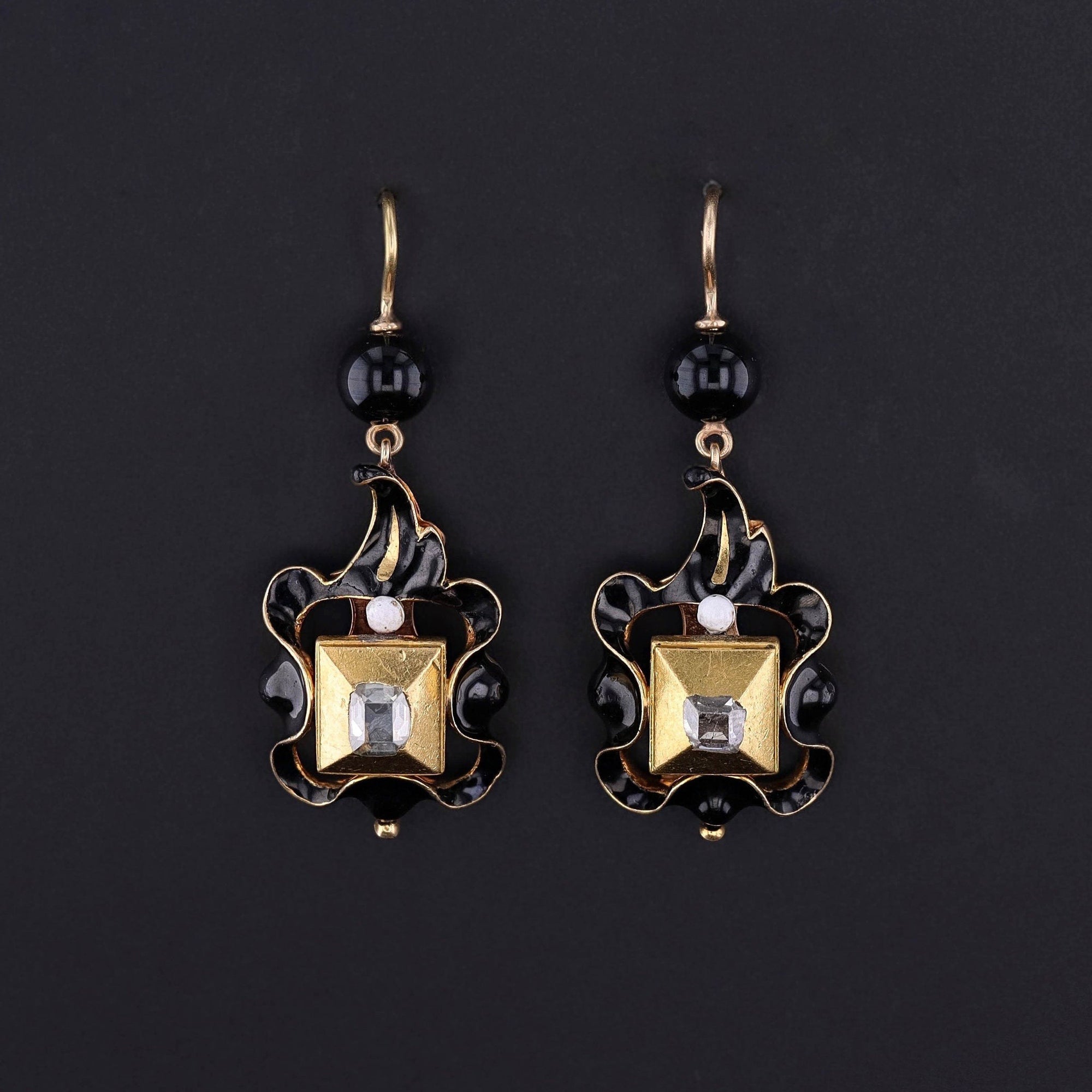 A rare pair of 17th century table cut diamond dangles in 22ct rub over settings with 18k black and white enamel drops, leaded glass bead surmounts, and 14k gold ear wires.