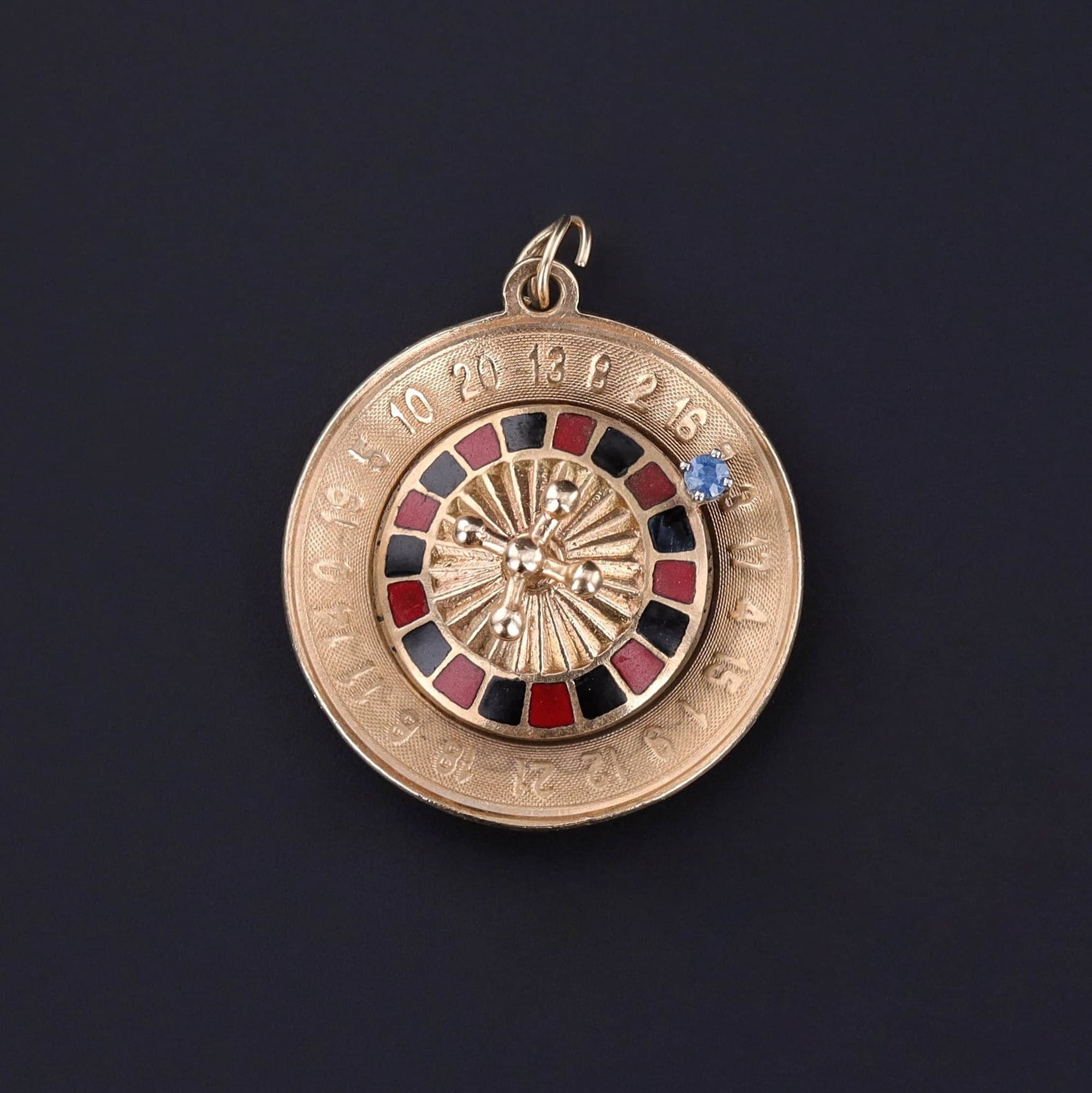 A perfect gift for a someone with a love of casinos or gambling. The 14k gold piece features a roulette wheel adorned with vibrant red and black enamel detailing and accented by a sparkling blue sapphire.