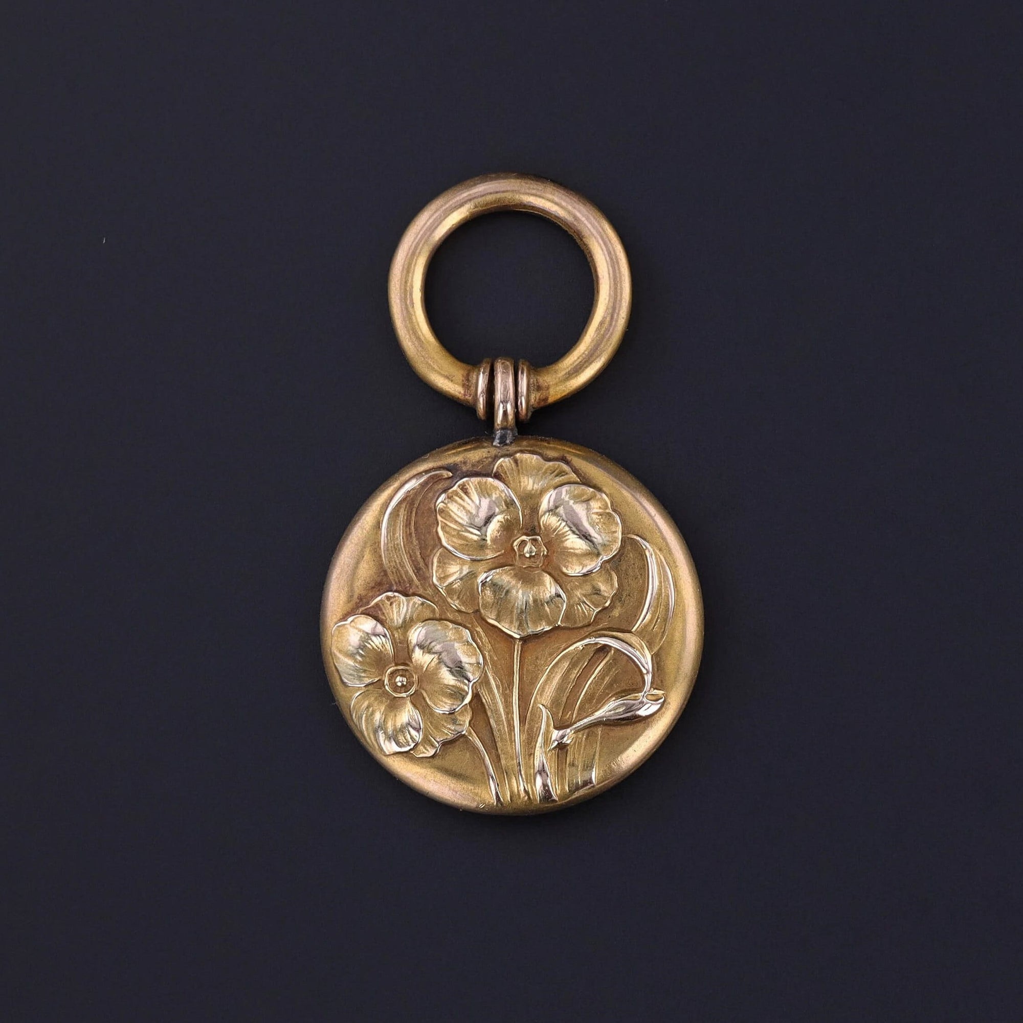 A floral treasure from the turn of the 20th century. This 10k gold pendant is embossed with a floral design on the front and a large bolt ring for dramatic effect. The reverse bears the inscription &#39;F. R. of Beunos Ayres (Aires) May 1904&#39;.