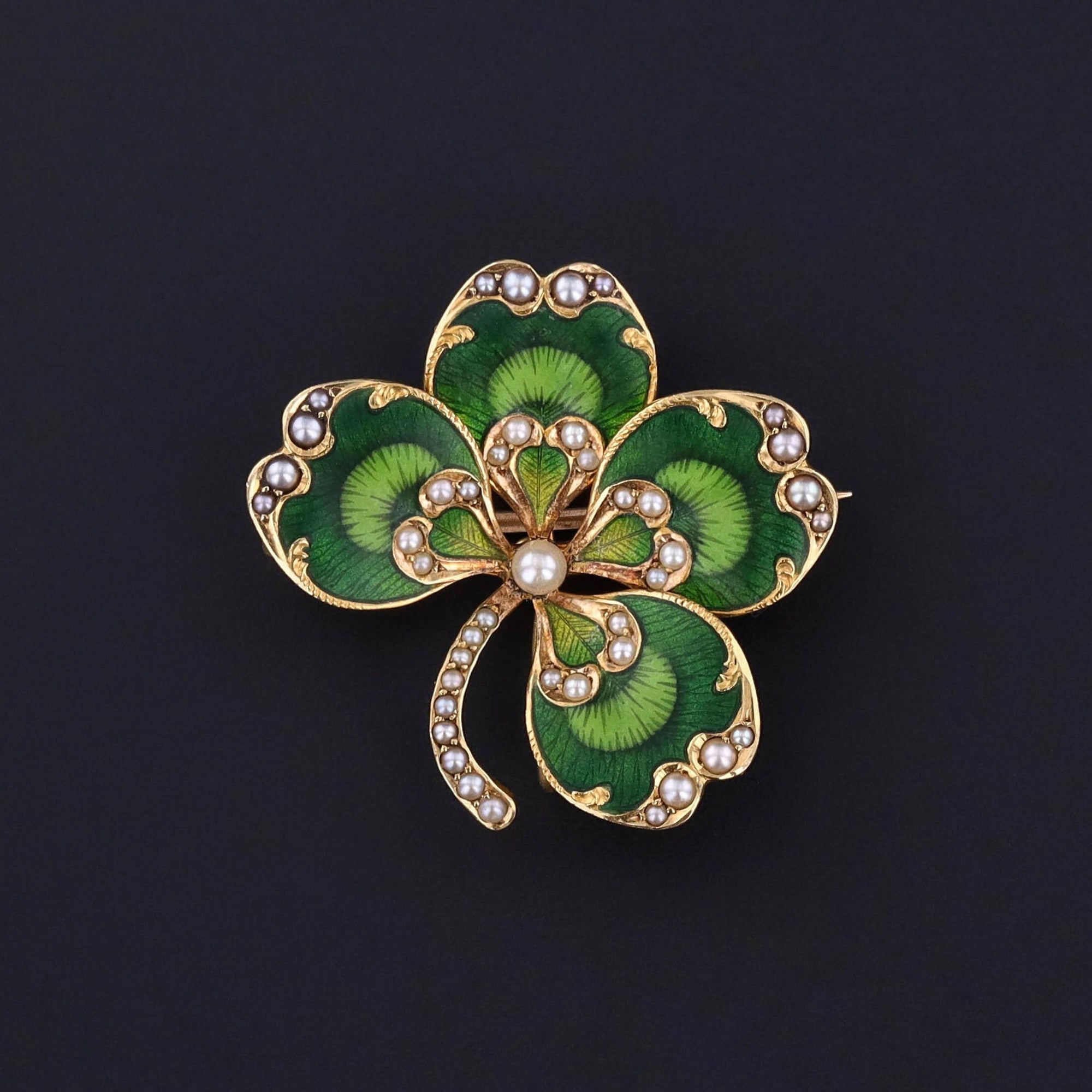 A striking antique clover dating to the early 1900s. The piece is adorned with vibrant green enamel and lustrous half pearls. It bears a pin and a collapsible bail allowing it to be worn either as a brooch or a pendant.
