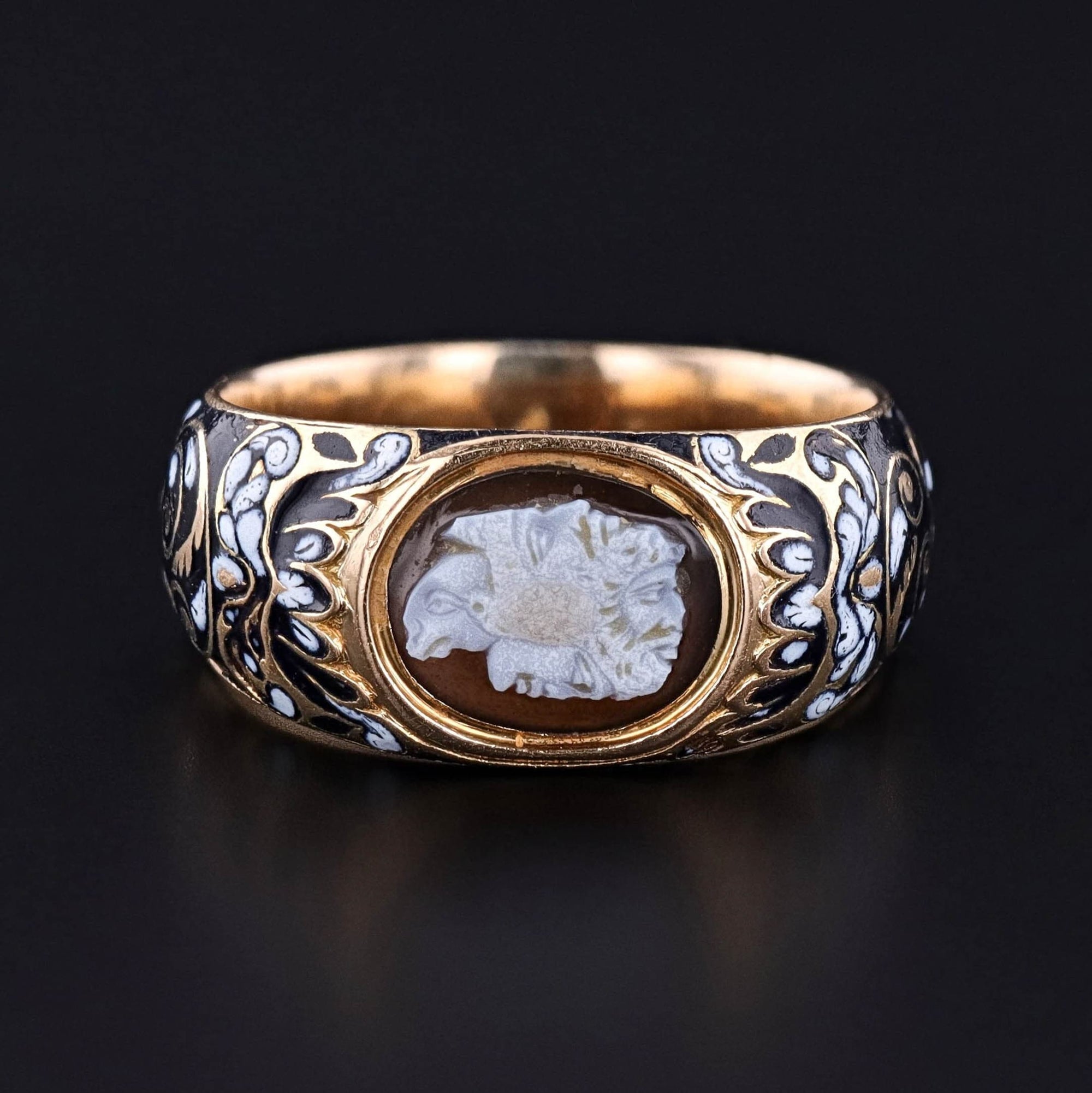 Explore the exquisite craftsmanship of this Renaissance revival ring (circa 1850), featuring a cameo of a gryllos, a multi-headed animal and human composite set in a substantial 18k gold mounting adorned with hand painted black and white enamel.