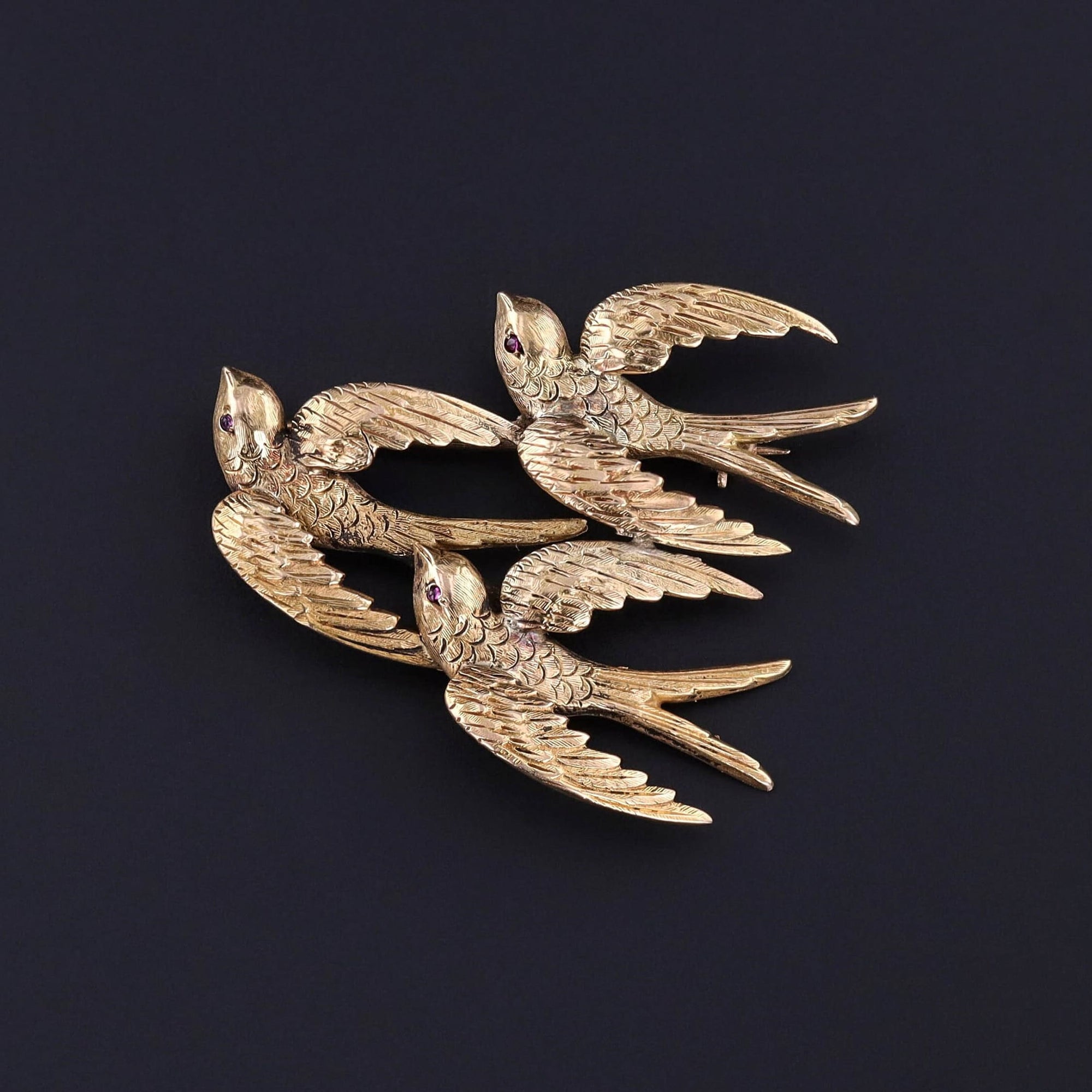 A late Victorian era 14k gold swallow brooch. Swallows are a symbol of homecoming and make wonderful bridal gifts. Each swallow has a tiny ruby eye.