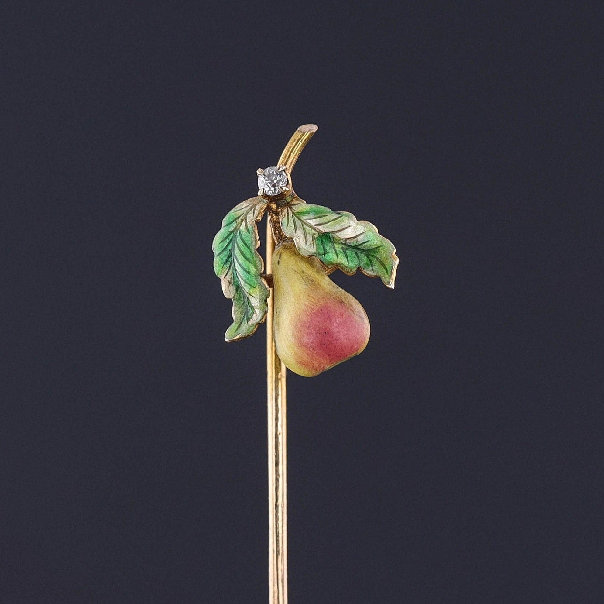 Antique Pear Stickpin: A vibrant antique pear stickpin (circa 1910) adorned with enamel and a sparkling diamond accent. The pin head measures 0.6 inches by 0.5 inches wide with the entire pin length measuring 2.3 inches long.