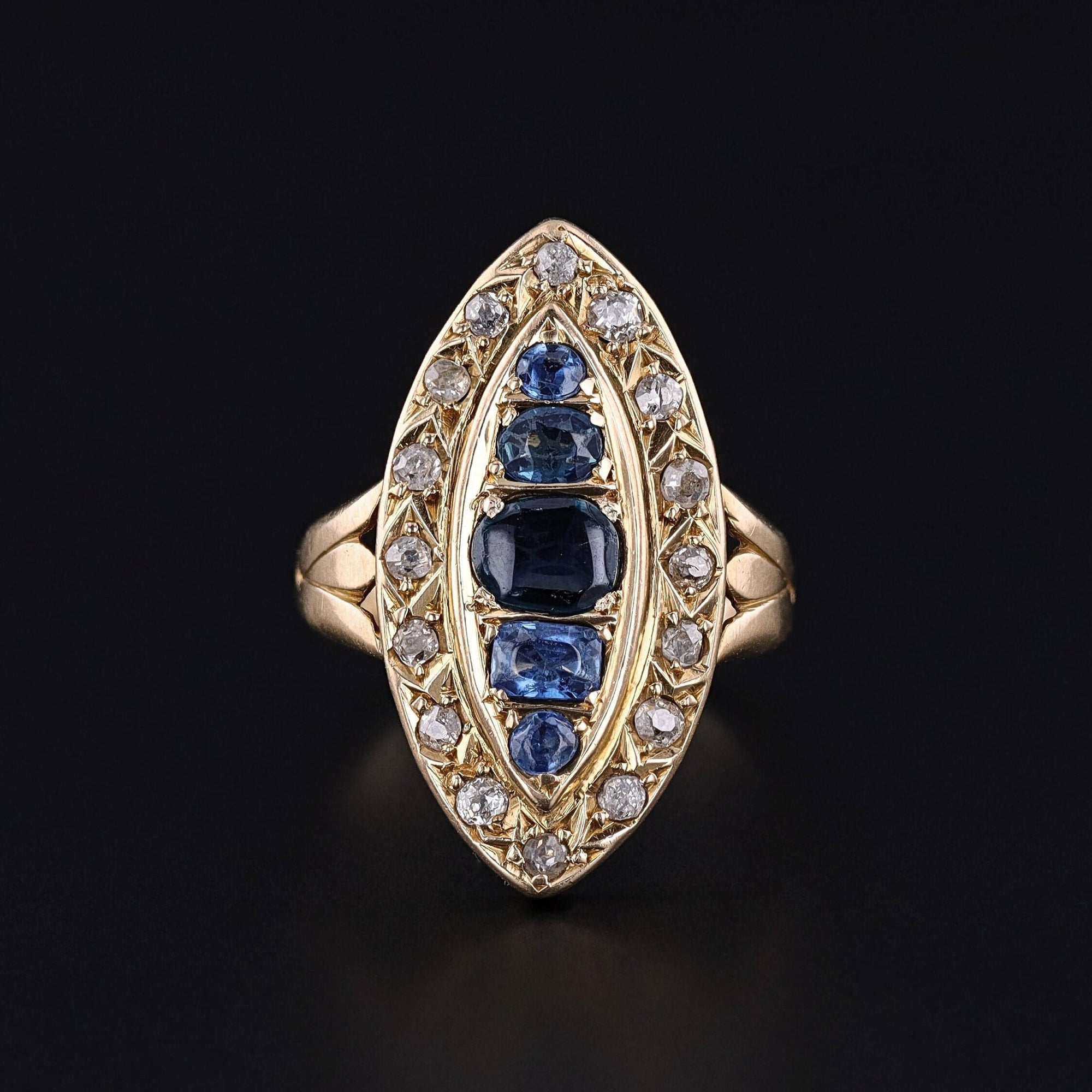 An antique ring from the late Victorian era showcasing a stunning navette design adorned with natural sapphires and old single cut diamonds mounted in 18k . The ring bears hallmarks indicating that it was assayed in Birmingham, England in 1893.
