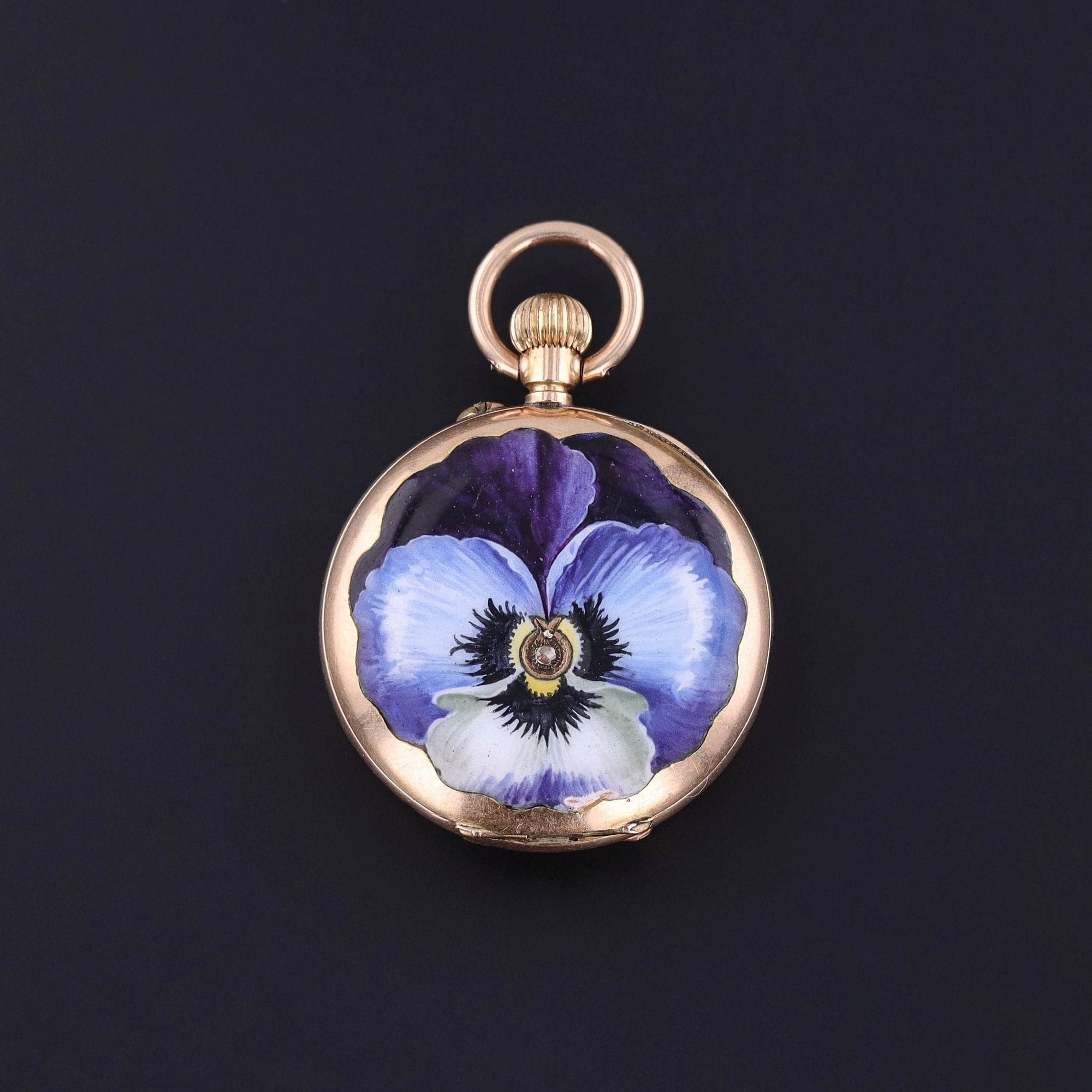 An antique enamel pocket watch adorned with a vibrant purple and white pansy. The 14k gold watch is fully functional and dates to the late 1800s to early 1900s. It is in very good condition and perfect for any watch or jewelry collector.