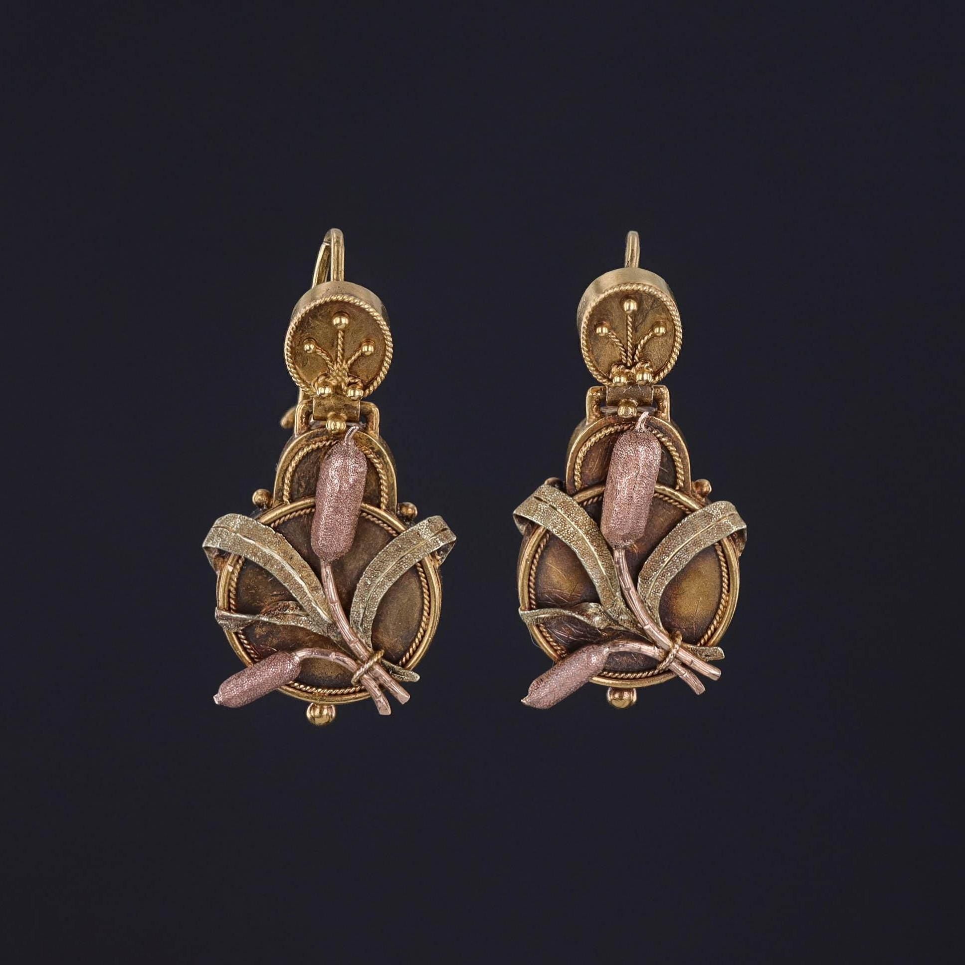 Each earring features textured leaves and cattail-like elements in a mix of pink and yellow gold.