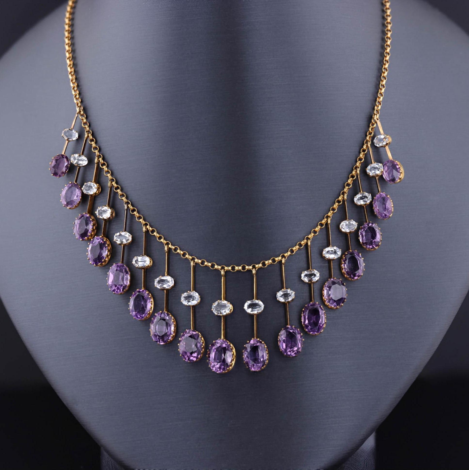 An antique necklace with alternating oval amethyst and diamond gemstones set in gold, creating a cascading effect. The gemstones are suspended from a fine chain, with larger amethysts toward the center.