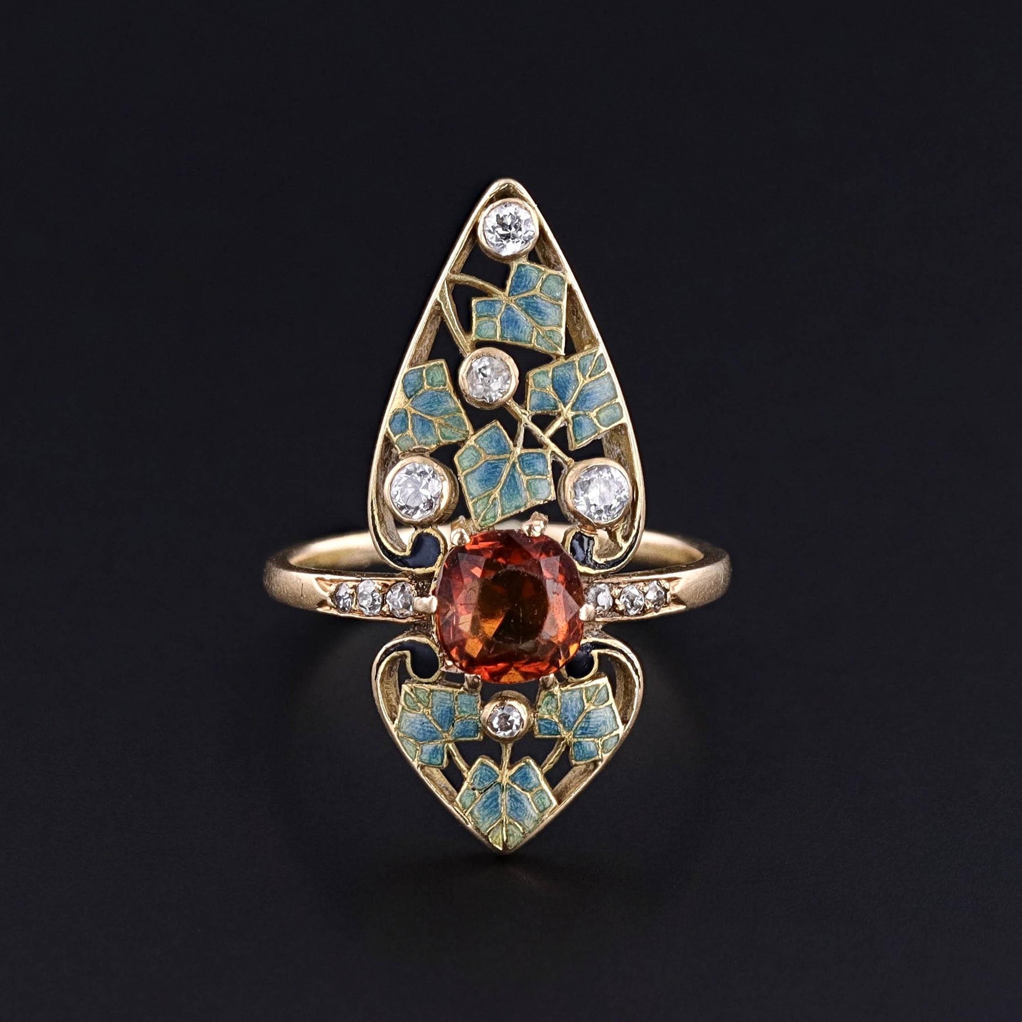 Front view of an antique gold ring featuring intricate blue enamel leaves, set with a central citrine stone and accented by  diamonds.