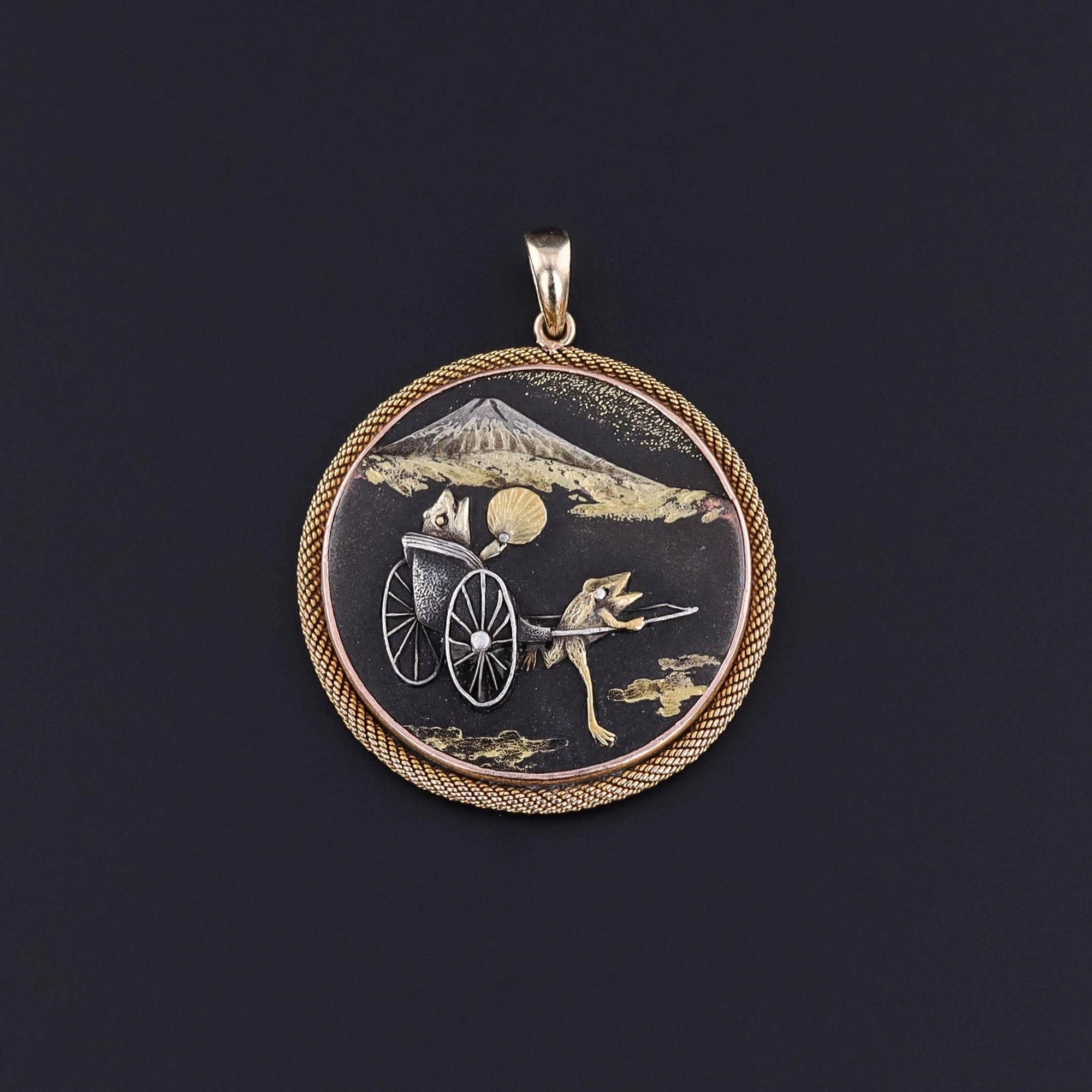 An antique Japanese shibuichi pendant depicting frogs in a rickshaw near a mountain.  It is mounted in 14k gold and 12ct gold.  It&#39;s similar to shakudo.