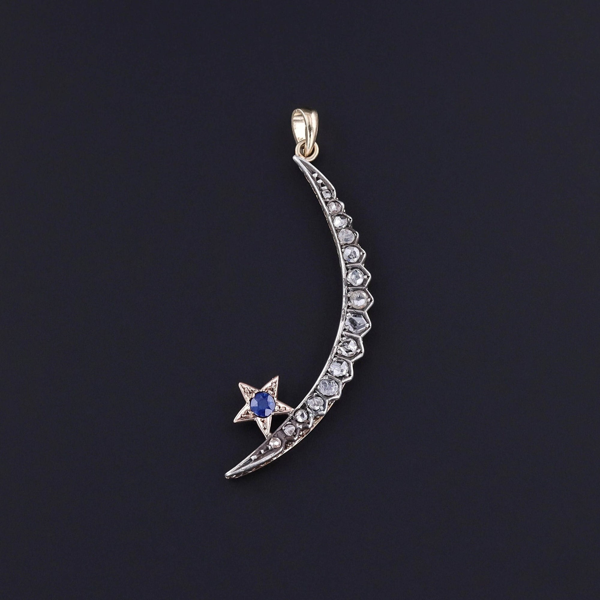 Antique diamond crescent moon pendant featuring rose-cut diamonds and a natural, untreated blue sapphire. It measures 2 inches in length by 0.6 inches in width. Perfect for vintage jewelry enthusiasts